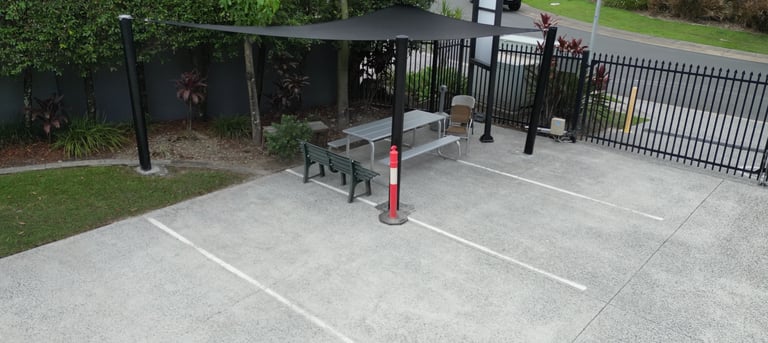 Outdoor parking area with metal benches, red bollard, and black metal fence surrounding landscaped grounds