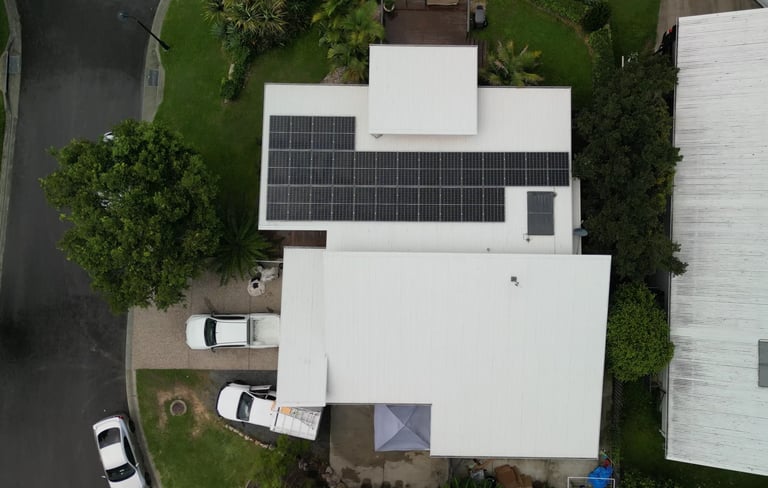 Aerial view of a modern white house with solar panels on the roof, surrounded by green landscaping and parked vehicles
