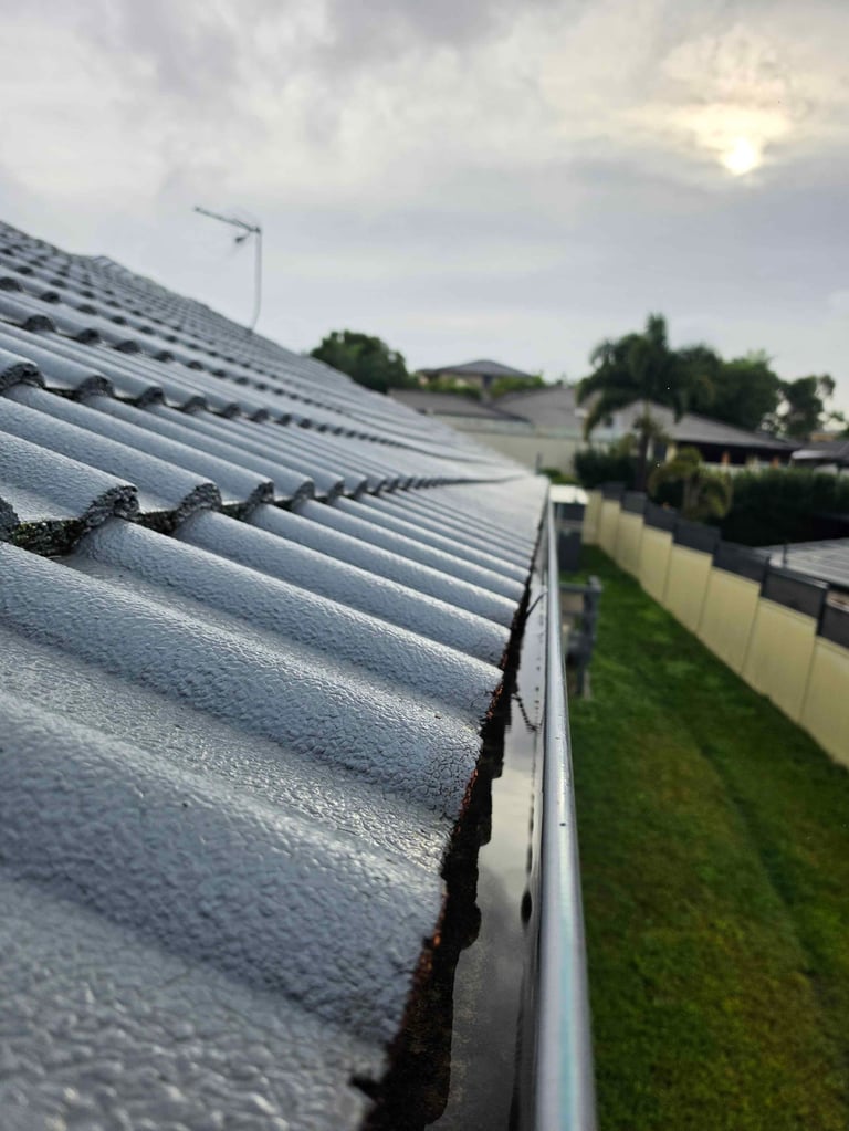 Close-up of wet corrugated metal roof gutters with residential houses and fenced yard in the background