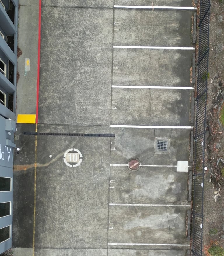Overhead view of an empty urban alley with gray concrete, striped parking spaces, and brick buildings on the sides