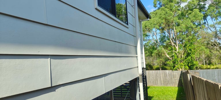 Modern house exterior with horizontal siding and large windows, bordered by wooden fence and green trees
