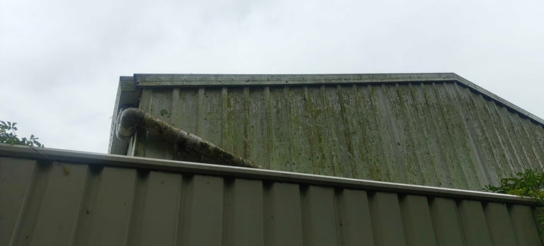Weathered metal industrial roof with corrugated panels and moss growth under overcast sky