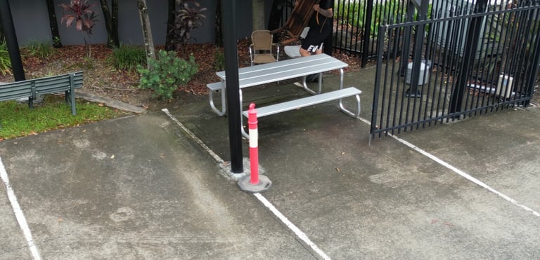Outdoor picnic area with a metal picnic table and bench on concrete ground, next to a black metal fence and red fire hydrant