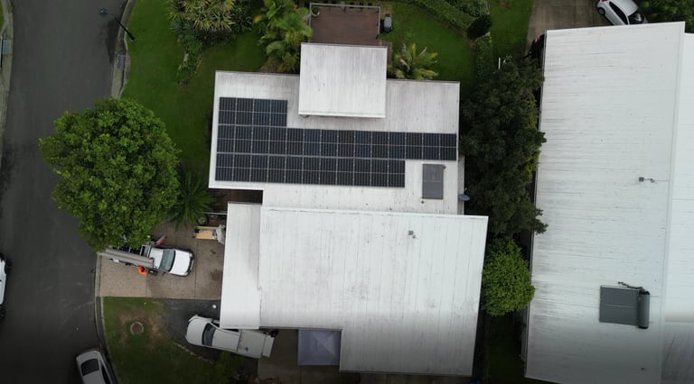 Aerial view of a residential roof with solar panels installed, surrounded by green landscaping and trees