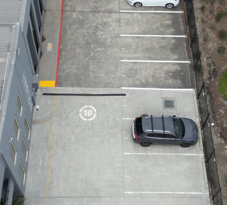 Overhead view of a parking lot with a black car in a numbered parking space and a white car visible in the background